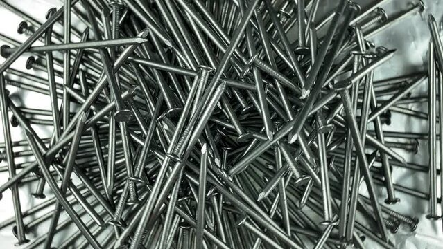 Directly above monochrome rotating pile of steel nails on silver foil at studio light. Metal hardware for construction site. Iron sharp details. Metallic repair material. Galvanized tacks carpenter