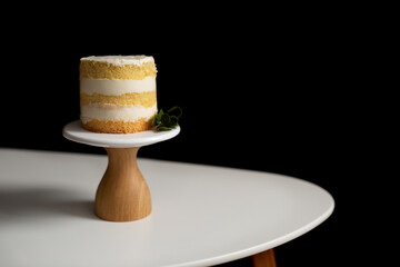 Holiday, celebration. A small cake on a stand on a white table on a black background