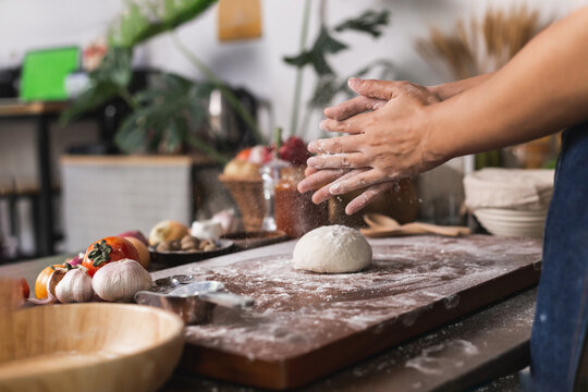 Close-up of a human hands kneading dough to make homemade pizza. Apron and hands knead the dough. Making dough by hand in a bakery. Preparing dought for pizza at home