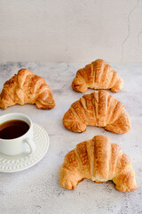 xícara branca com café puro e croissant assados sobre superfície branca com textura de cimento