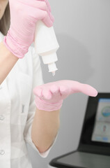  woman showing bottle with ultrasound guide gel for laser epilation procedure. drop of a gel on hand in protective rubber medical gloves. vertical.