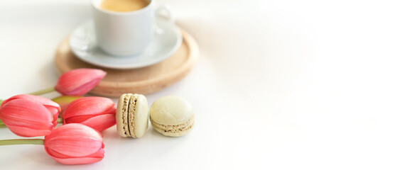 Obraz na płótnie Canvas Close up of sweet french macarons, cup of tea or coffee and spring flowers on white background. Space for text.
