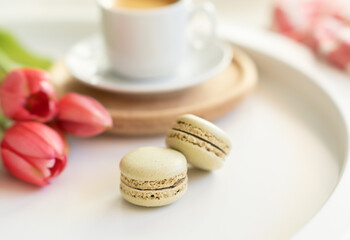Fototapeta na wymiar Close up of sweet french macarons, cup of tea or coffee and spring flowers on white background. Space for text.