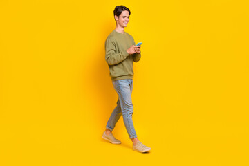Fototapeta na wymiar Full body profile portrait of positive person use telephone typing write walking isolated on yellow color background
