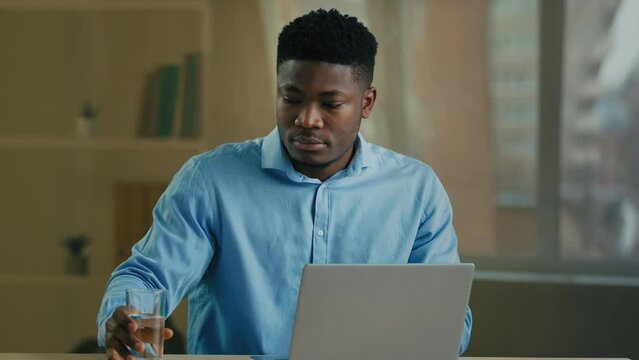 Businessman african american man working on computer in home office make pause drinking glass of cold fresh water health habit hydrate body mineral pure aqua drink recreation weight healthy metabolism