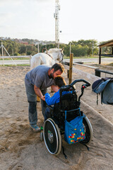 Kid in wheelchair outdoors in a horse ranch.