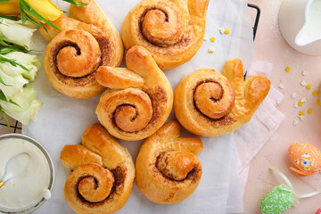 Easter breakfast Holliday concept. Easter bunny buns rolls with cinnamon made from yeast dough with orange glaze, easter decorations, colored eggs on pink spring background. Easter Holliday card.