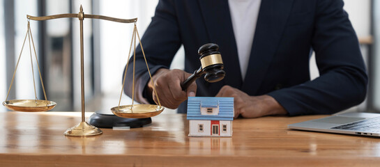 Fototapeta na wymiar Close-up of a house in front of a lawyer holding a hammer and a laptop silver brass scales on a wooden table in his office, law, legal services, advice, justice and real estate ideas.