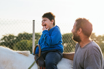 Child with disabilities enjoying having an equine assisted therapy in an equestrian center. - obrazy, fototapety, plakaty