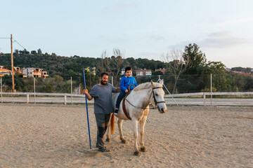 Happy kid with disabilities riding horse in an equine therapy session.