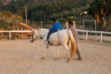 Kid with disabilities riding horse in an equine therapy session with a physiotherapist.