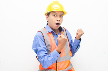 overjoyed asian male construction worker in blue shirt and orange vest with yellow safety helmet doing yes gesture by raising his fist.