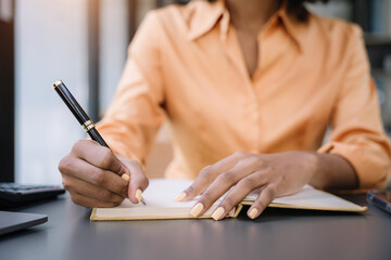 African young woman sitting and writing notes at desk in office.