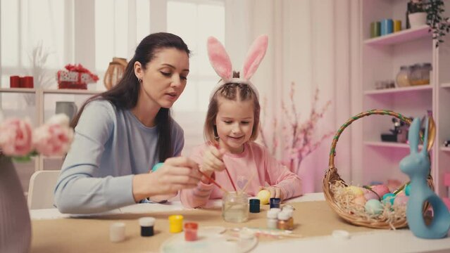 Young mother and her little daughter drawing designs on Easter eggs, holidays