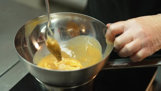Baker stirring yellow dough with metal tablespoon in a metal bowl and holding it. Blurred background. High quality 4k footage