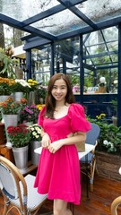 pink dressed woman posing in the garden outdoor of a café with multiple flowers behind her as background