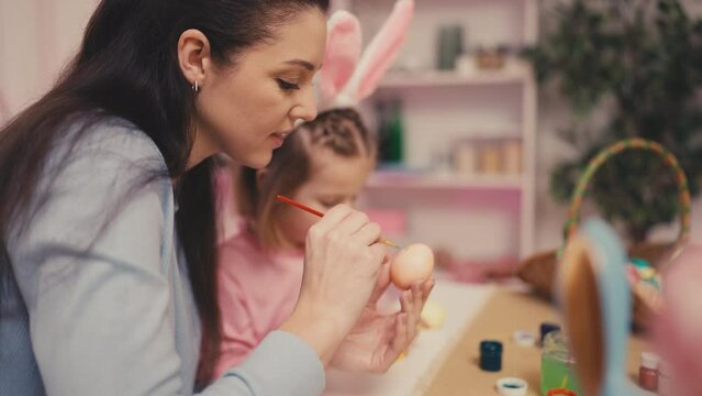Smiling girl in bunny ears and her mom decorating Easter eggs with ornaments