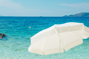 Fototapeta na wymiar white sun umbrella clear blue water on background