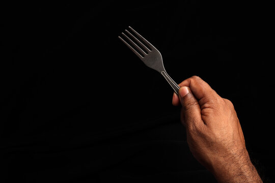 Asian dark skin top view two hand finger holding empty metal fork spoon on black background