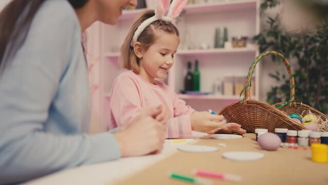 Young mother and little daughter coloring paper Easter eggs at home together