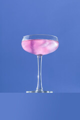 Minimal pink cocktail drink concept with ice in champagne glass on purple blue background. Party celebration aesthetic.