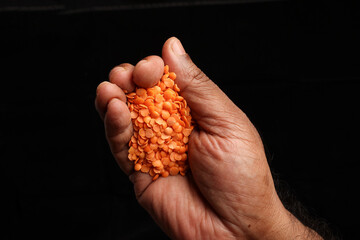 Asian dark skin top view two hand palm finger holding red lentil dahl on black background