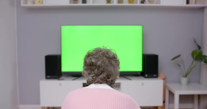 Old lady sits on a couch and turns on TV with greenscreen, chroma key4k