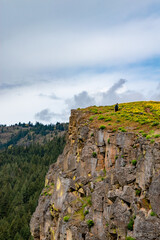 Fototapeta na wymiar Single Hiker Alone on Cliff on Cloudy Day in Spring at Coyote Wall in the Columbia River Gorge in Oregon & Washington