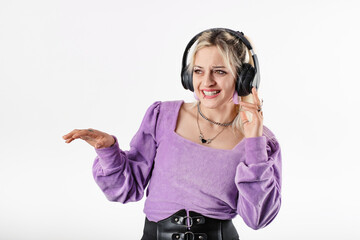 Cute caucasian woman wearing lilac ribbed blouse isolated over white background listens to music by touching headphones is having a lot of fun. Dj playing music.