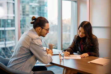 Asian resource manager going through paperwork with job candidate during meeting in office.