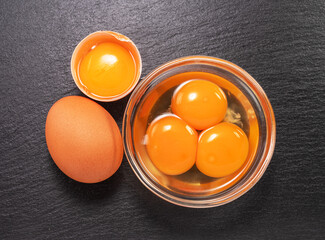 Brown chicken egg and egg yolks in glass bowl on natural stone black board. Flat lay.