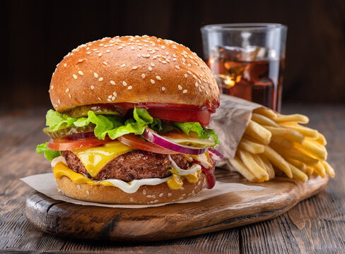 Tasty cheeseburger, glass of cola and french fries on wooden tray close-up.
