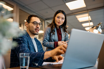 Multiracial colleagues cooperating while working on laptop in office.