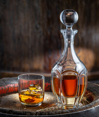 Carafe of whisky and glass of whisky on old wooden cask at the dark background.