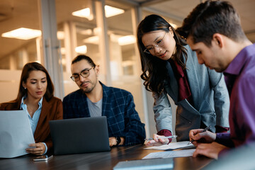 Asian businesswoman and her colleagues cooperate while working reports during meeting.