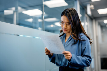 Asian female entrepreneur analyzing business reports in office.