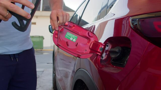 Static shot of crop man in causal clothes opening tank door of red car and removing lip then putting nozzle of pump inside