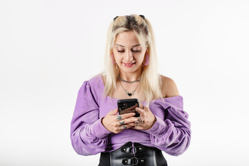 Fototapeta premium Happy woman wearing ribbed blouse standing isolated over white background holding a phone and looking at the screen. Smiling, texting with boyfriend. Using mobile phone, typing sms message.