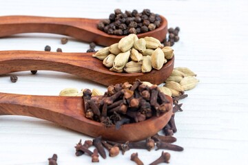 Cardamon, Cloves, and Black Pepper in Wooden Sppos Isolated on White Background with Selective Focus on Cardamom