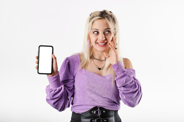 Blonde woman standing isolated over white background delighted, holds the phone with one hand, touches cheek and looks at the empty copy space. Very happy, sees a great discount or a great deal.