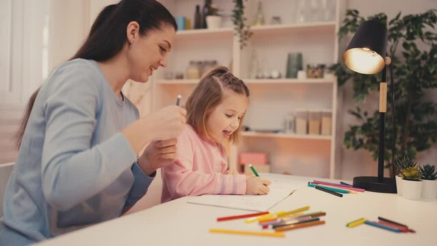Smiling girl and her young mom having fun while drawing, family togetherness