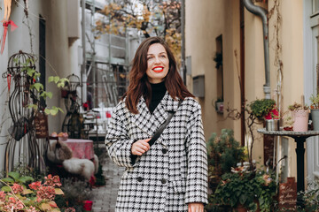 A beautiful brunette in an coat walks through an old courtyard decorated with potted plants