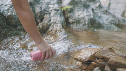 Hand holding a water bottle and was drawing water in the forest river or waterfall