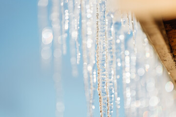 Photo of icicles on the rooftop on the backgrounf blue sky under warm sunlight on the winter, it's shining on a sun. Wintertime and springtime atmosphere with warm sunlight.