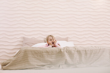 Morning of little girl in a comfortable bedroom. Happy child girl having fun and plays in bed