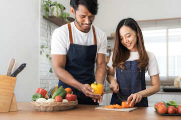 Romantic couple is cooking on kitchen. Handsome man and attractive young woman are having fun together while making salad. Healthy lifestyle concept.