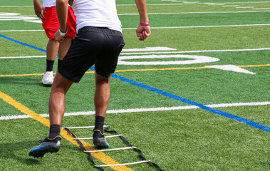 Football player running in the ladder drill with his coach watching