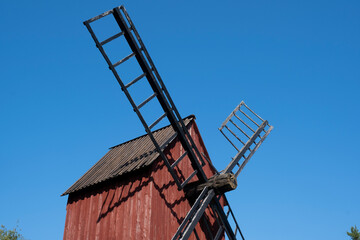 And old red windmill with wooden blades against a bright blue sky