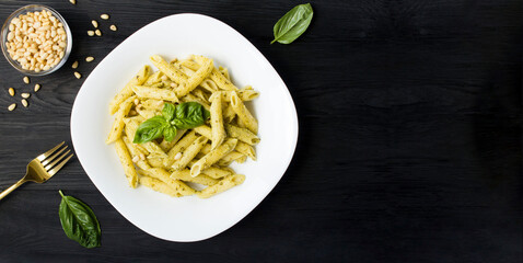 Italian pasta with pesto and pine nuts in the white plate on the black wooden background. Top view. Copy space.
