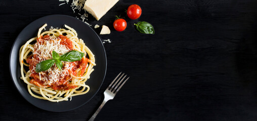 Italian pasta with tomato sauce and parmesan in the black plate on the black wooden background. Copy space. Top view.